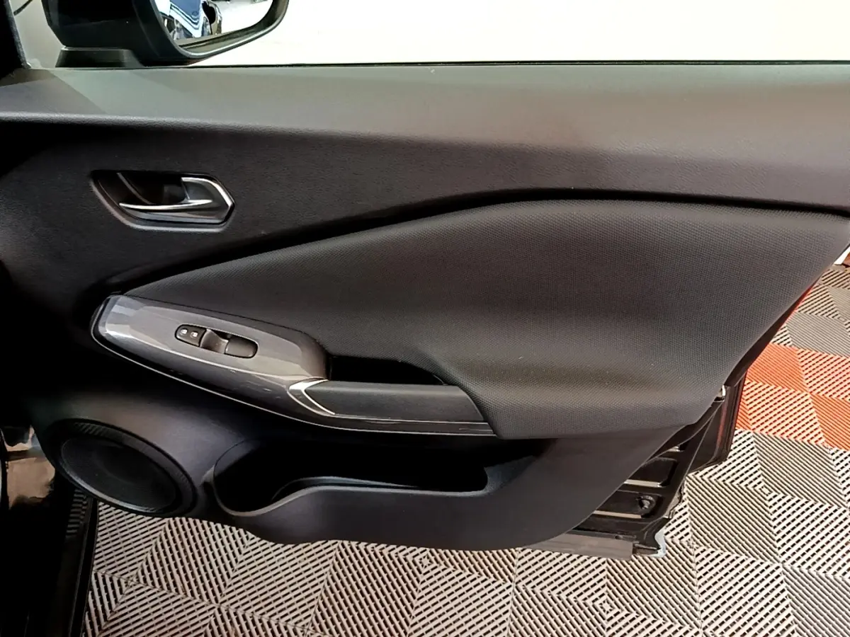 Vue intérieure du panneau de porte côté conducteur noir du Nissan Juke 2023 avec commandes de vitres et haut-parleur intégré.