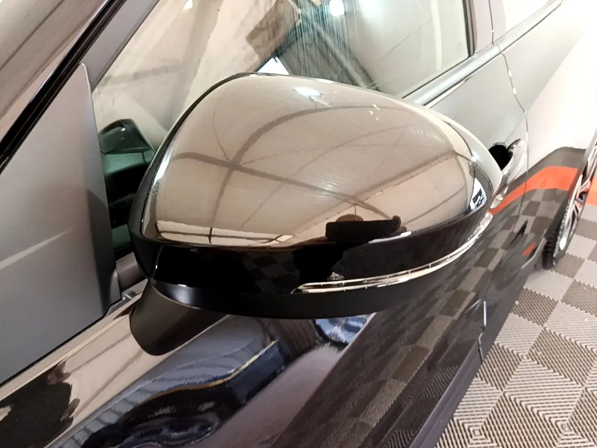 Gros plan sur le rétroviseur droit noir brillant du Nissan Juke 2023, avec reflet du plafond et carrosserie noire visible.