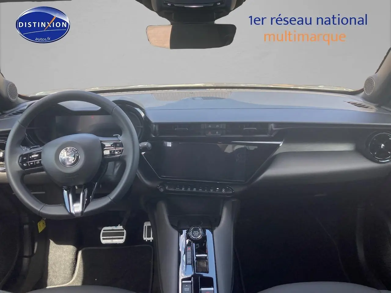 Vue intérieure avant de l'Alfa Romeo Junior 1.2 hybride gris, tableau de bord moderne avec écran tactile et volant multifonction.