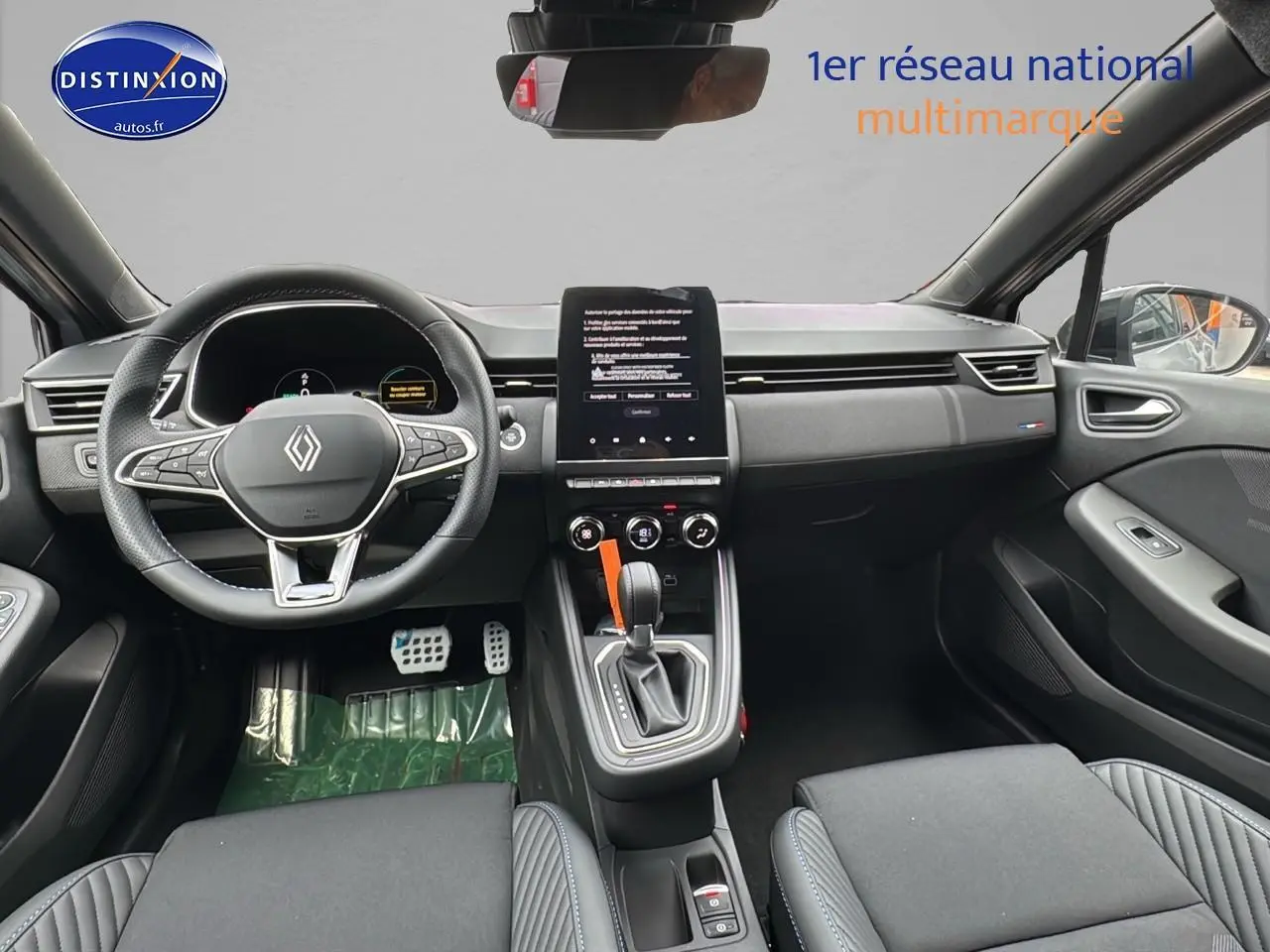 Vue intérieure avant de la Renault Clio V gris rafale, volant multifonction, écran tactile vertical et levier de boîte auto.