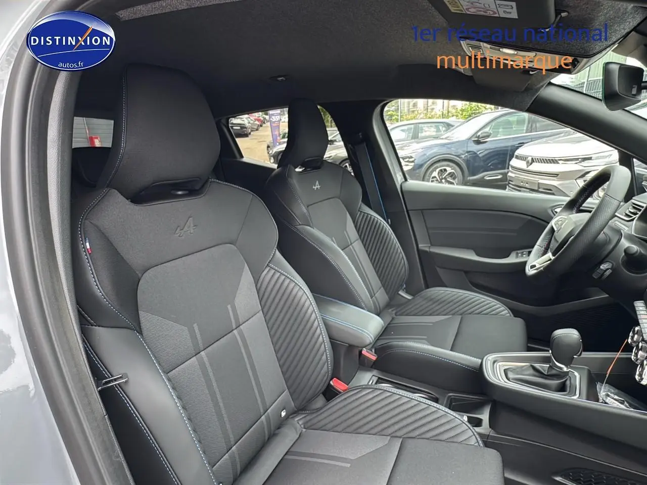 Intérieur avant de la Renault Clio V gris rafale, sièges sport esprit Alpine avec surpiqûres bleues et accoudoir central.