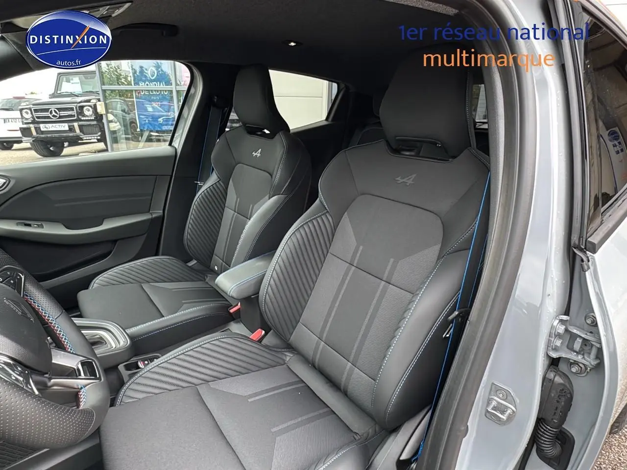 Vue intérieure côté droit de la Renault Clio V gris rafale, sièges sport esprit Alpine avec surpiqûres bleues et accoudoir central.