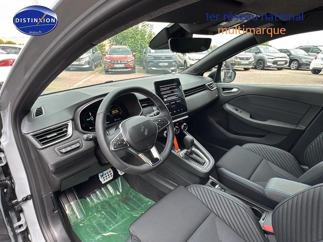 Intérieur avant de la Renault Clio V gris rafale, volant multifonction et écran tactile central visible depuis la porte ouverte côté conducteur.