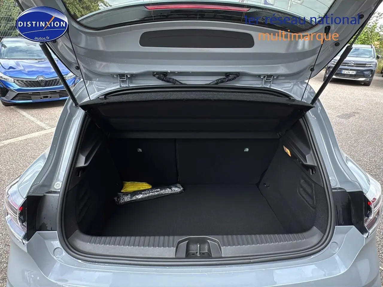 Coffre ouvert vu de l'arrière d'une Renault Clio V gris rafale, avec intérieur noir et accessoires rangés.