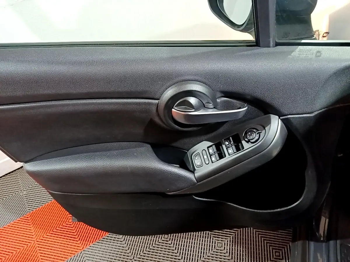 Gros plan sur la porte côté conducteur noire de la FIAT 500X avec commandes électriques des vitres et poignée argentée.