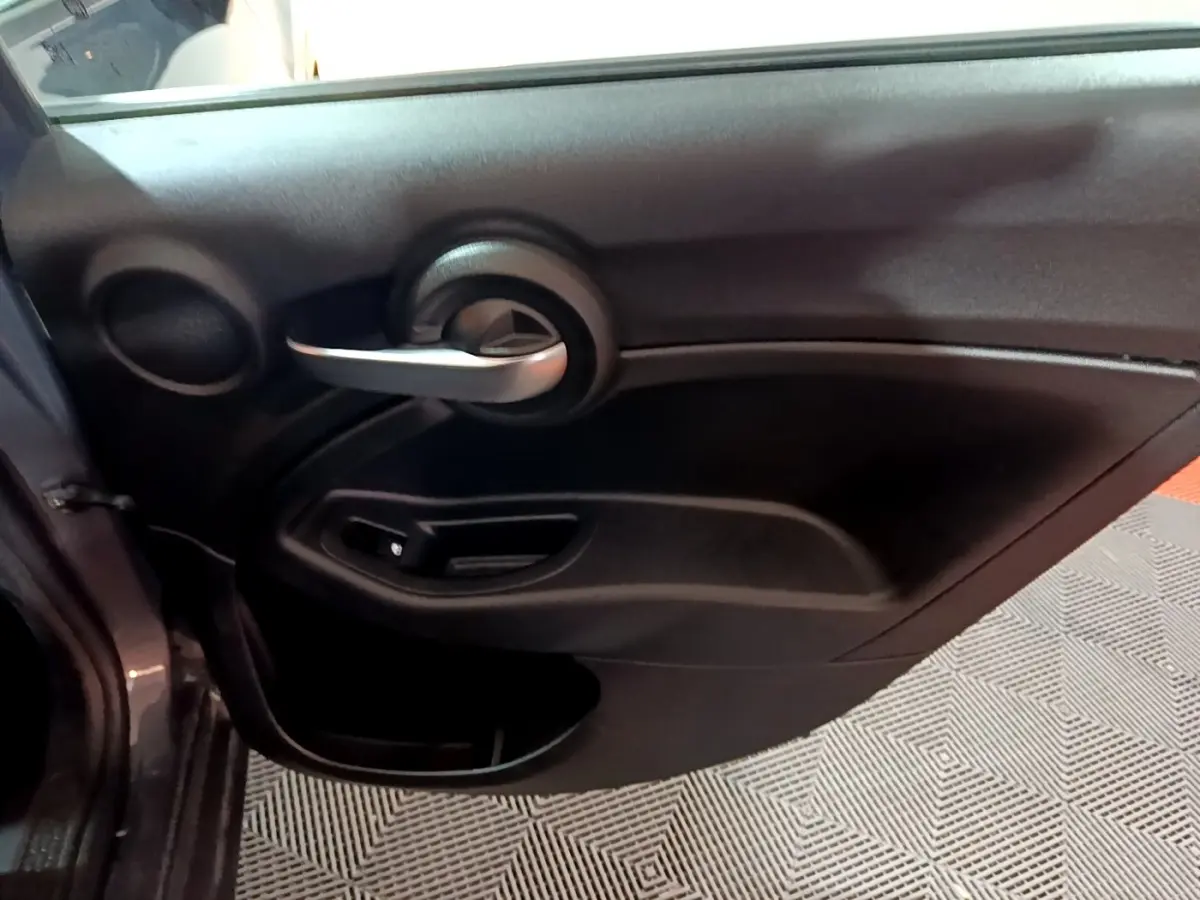 Vue rapprochée de la porte intérieure côté gauche gris foncé du FIAT 500X 2019 avec poignée argentée et commande de vitre.