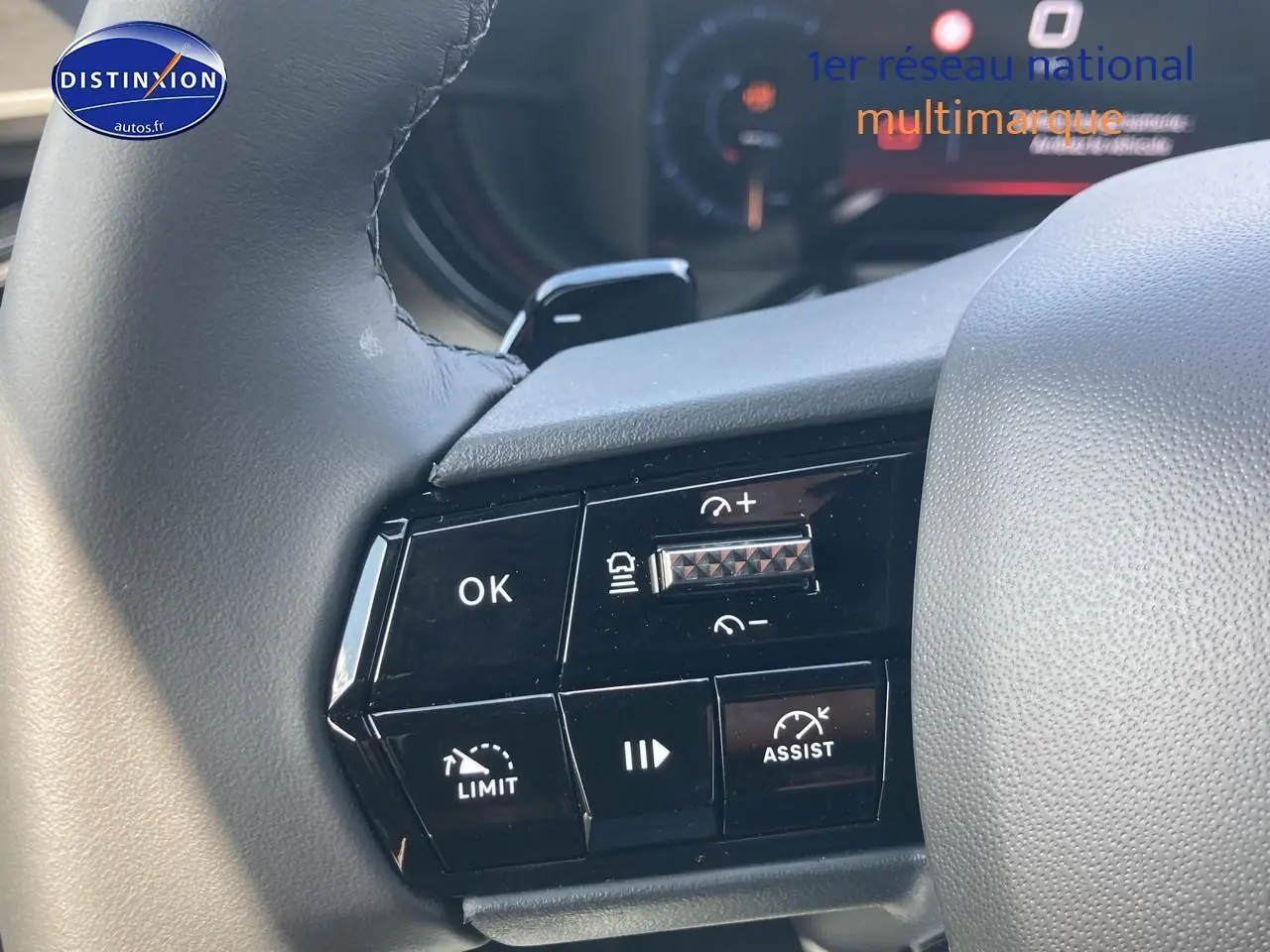Gros plan sur les commandes au volant noir de l'Alfa Romeo Junior 1.2 hybride, mettant en valeur les boutons d'assistance et régulateur.