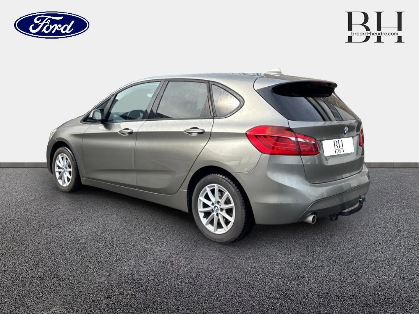 BMW Série 2 Active Tourer 216dA grise vue 3/4 arrière droit, avec jantes alu et attelage visible.