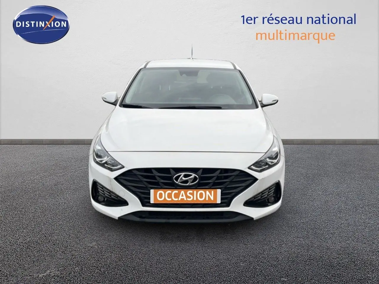 Vue de face d'une Hyundai i30 blanche nacrée avec calandre noire et plaque "OCCASION" orange.