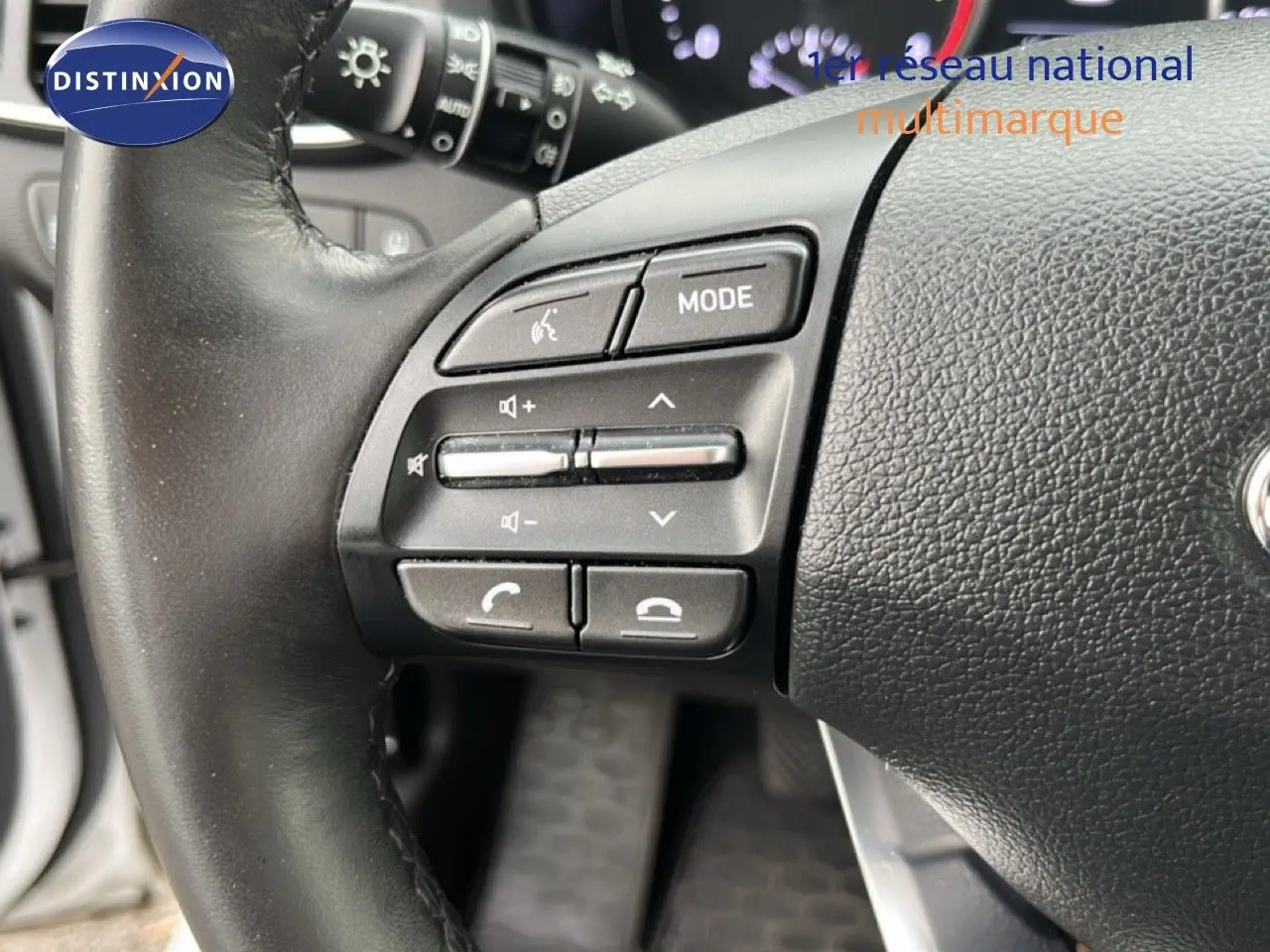 Gros plan sur les commandes gauche du volant noir d'une Hyundai i30 blanche nacrée, mettant en valeur les boutons multifonctions.