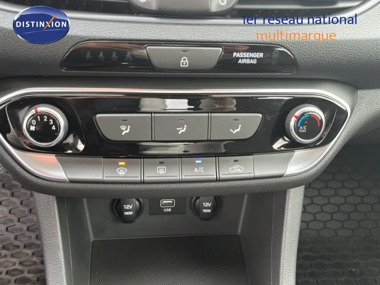 Vue rapprochée de la console centrale de la Hyundai i30 blanche nacrée, montrant les commandes de climatisation et ports USB et 12V.