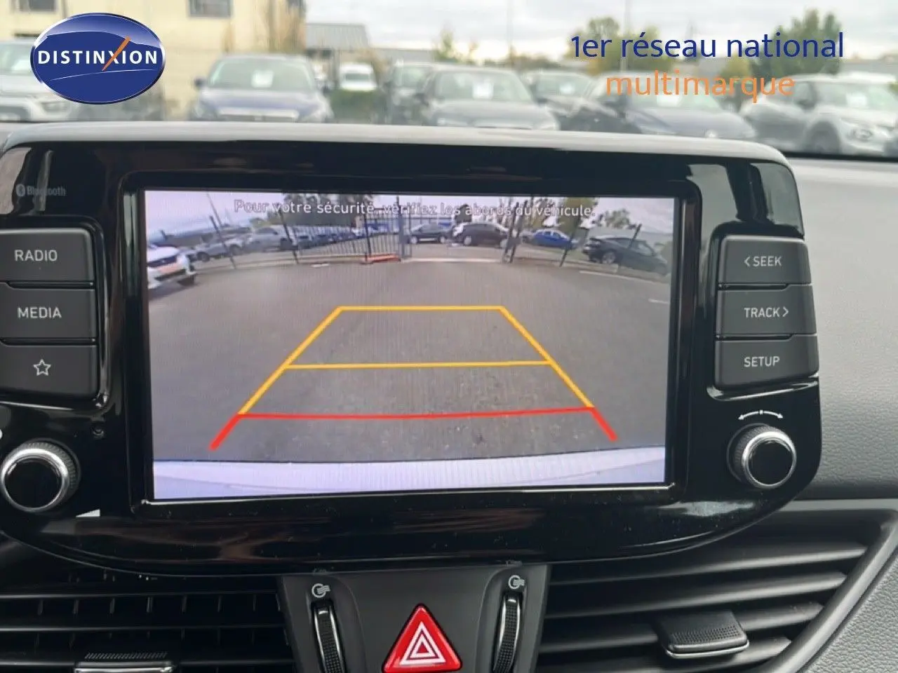 Écran central de la Hyundai i30 blanc nacré 2023 montrant la caméra de recul avec lignes de guidage colorées.