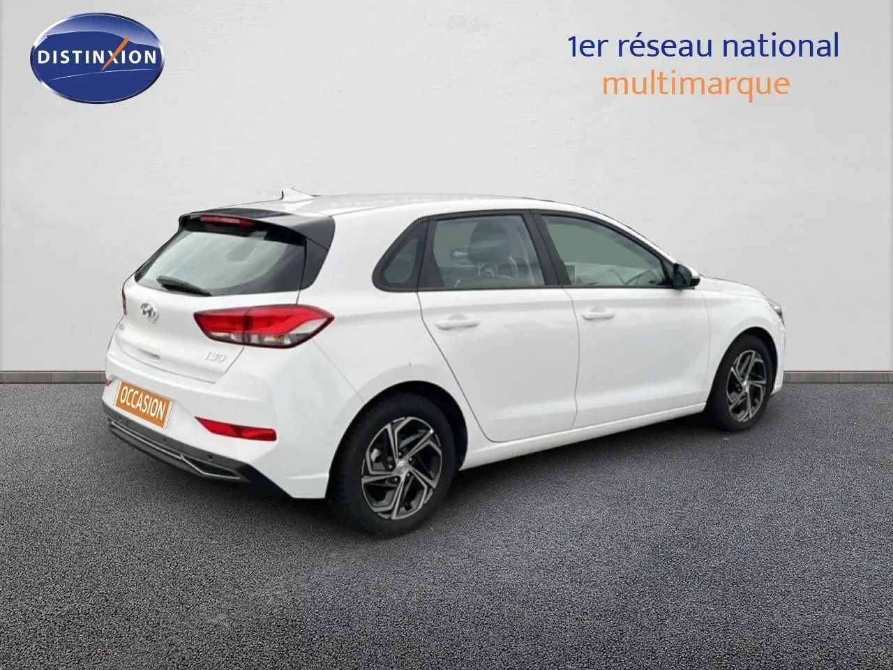 Vue 3/4 arrière droite d'une Hyundai i30 blanc nacré 2023, compacte 5 portes avec jantes alliage bicolores.