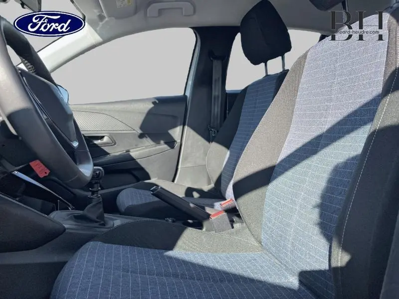 Vue intérieure côté conducteur montrant les sièges tissu bleu et noir et la boîte manuelle d'une Peugeot 208 AFFAIRE blanche