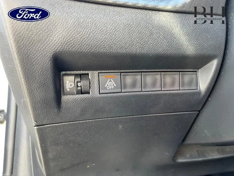 Gros plan sur les commandes de réglage des phares et désactivation de l'aide au maintien de trajectoire dans un Peugeot 208 Blanc Banquise.
