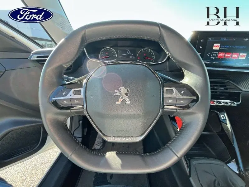 Vue rapprochée du volant cuir noir de la Peugeot 208 Affaire 2022 avec commandes intégrées et tableau de bord digital.