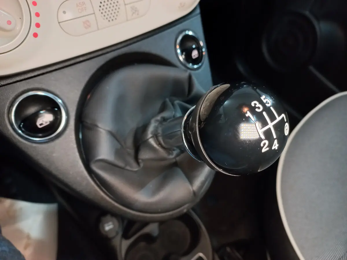 Gros plan sur le levier de vitesses manuel noir de la Fiat 500 Lounge, avec console centrale et sièges partiellement visibles.