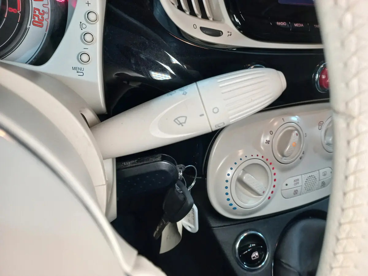 Détail intérieur côté gauche montrant la commande d’essuie-glace et les réglages de climatisation sur tableau de bord noir et beige.