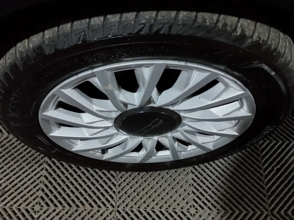 Gros plan sur la jante argentée d'une FIAT 500 noire, mettant en valeur le logo central distinctif.