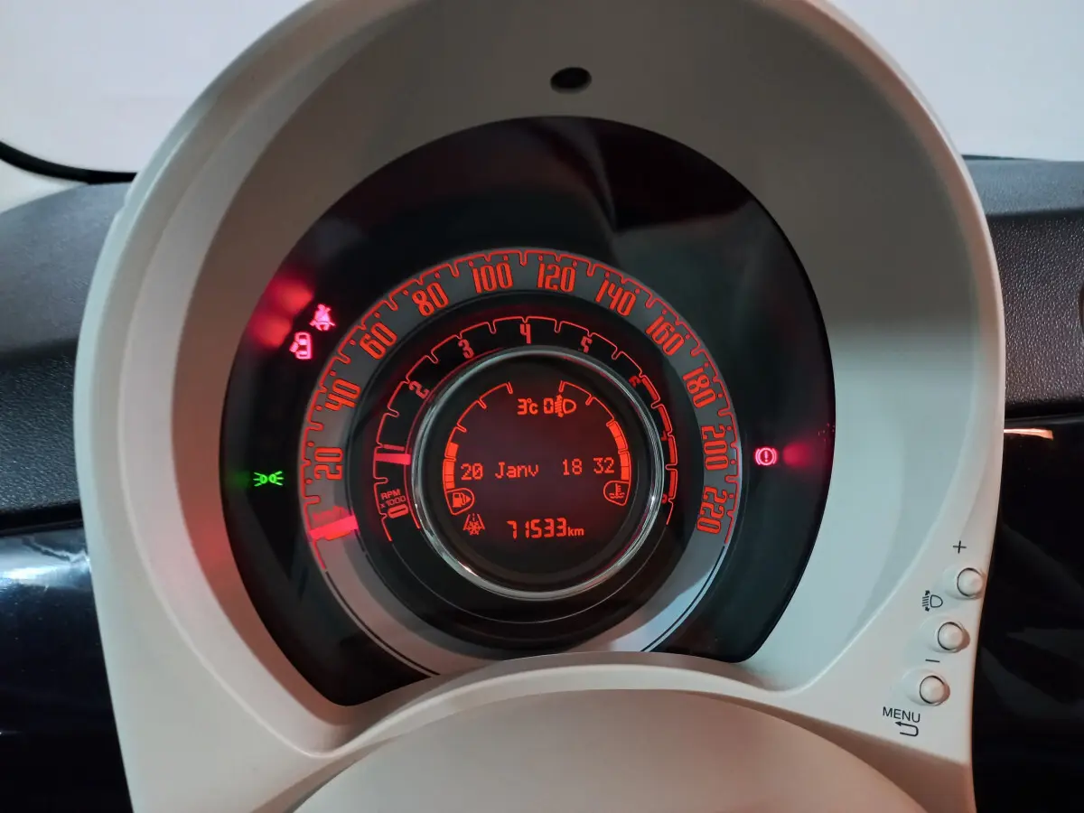 Gros plan sur le tableau de bord circulaire de la Fiat 500 noire, avec affichage digital rouge et indicateurs lumineux allumés.