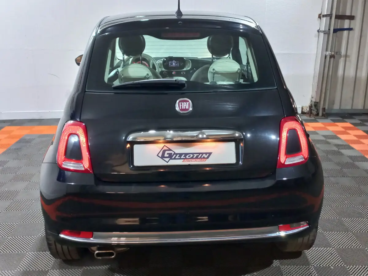 Vue arrière d'une FIAT 500 noire 2018 avec feux arrière allumés et plaque d'immatriculation encadrée chromée.