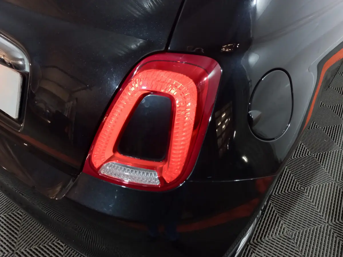Gros plan sur le feu arrière droit rouge d'une FIAT 500 noire, avec trappe à carburant visible sur le côté droit.