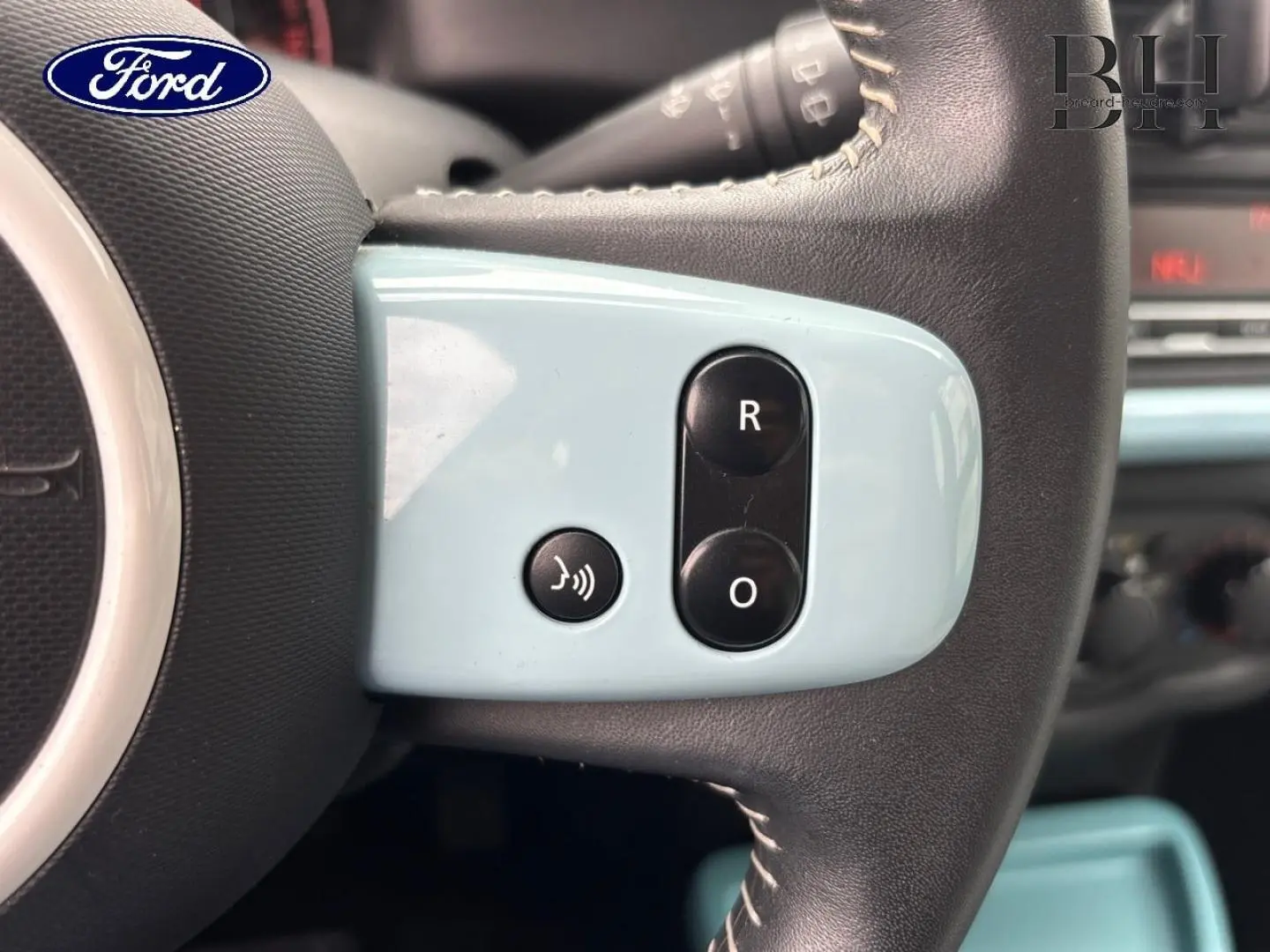 Gros plan sur les commandes bleues du volant d’une Renault Twingo 2014 Bleu Dragée, côté gauche.