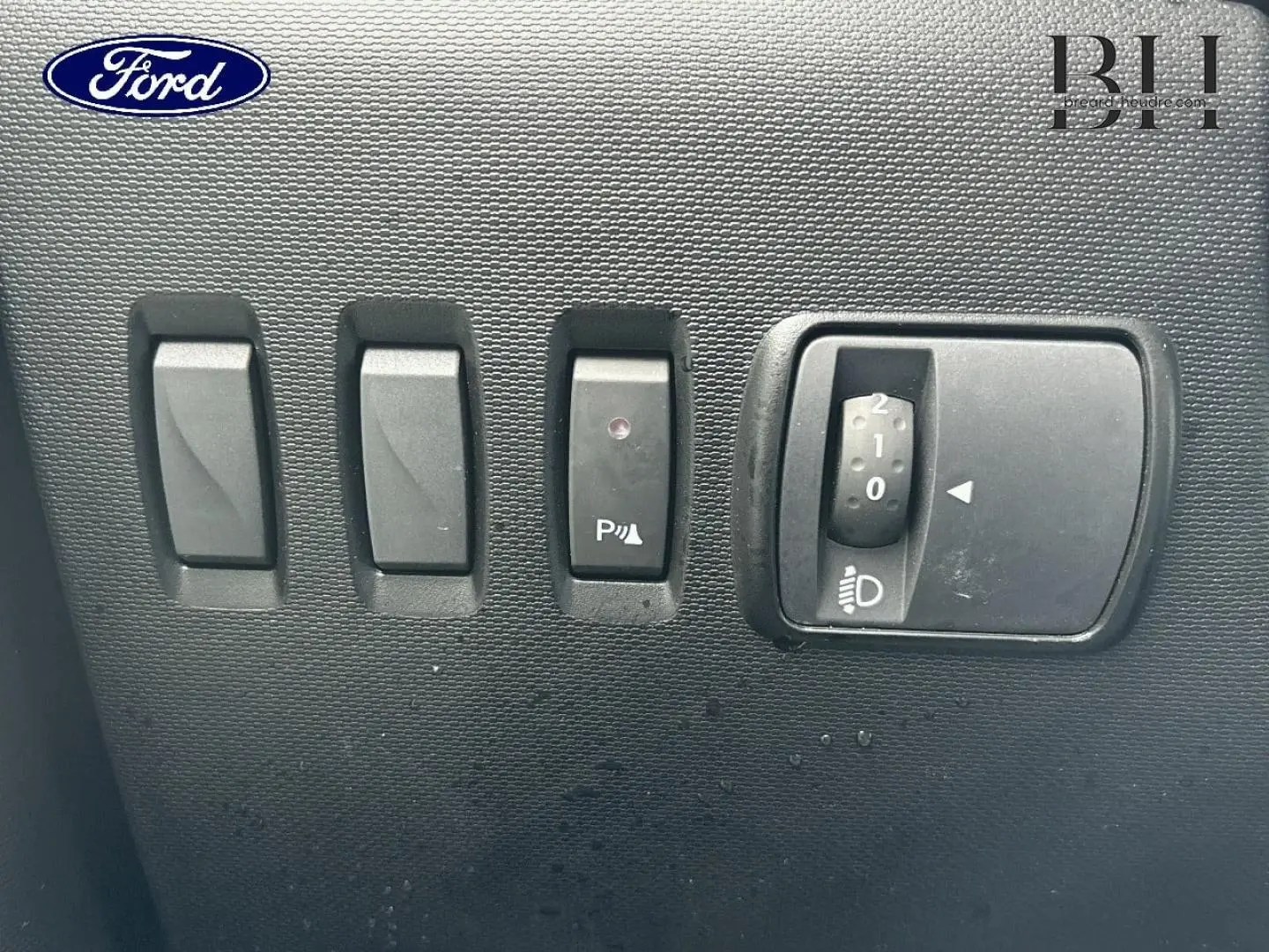 Gros plan sur les commandes de réglage des phares et de l'aide au stationnement d'une Renault Twingo bleu dragée.