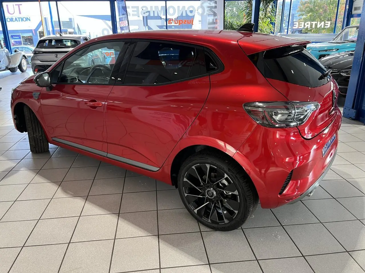 Renault Clio 2024 rouge vue 3/4 arrière droit avec jantes noires et vitres surteintées en showroom.