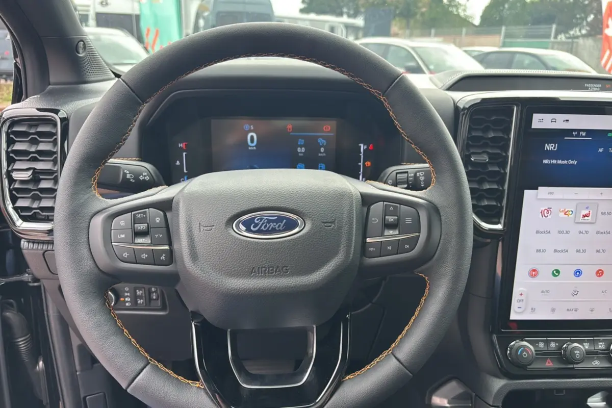 Vue intérieure centrée sur le volant noir du Ford Ranger 2025 Wildtrak Plus avec tableau de bord digital et écran tactile.