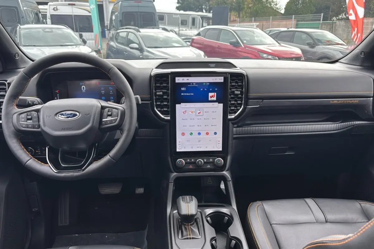 Vue intérieure du tableau de bord du Ford Ranger Wildtrak Plus 2025 noir agate avec écran tactile vertical et coutures orange.