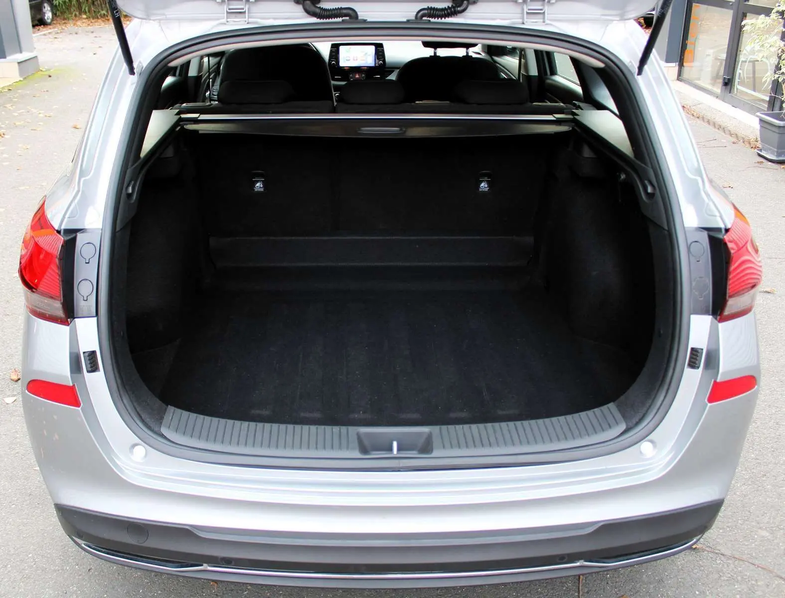 Coffre ouvert vu de l'arrière d'une Hyundai i30 SW 2024 en argent brillant, montrant un espace de chargement spacieux.