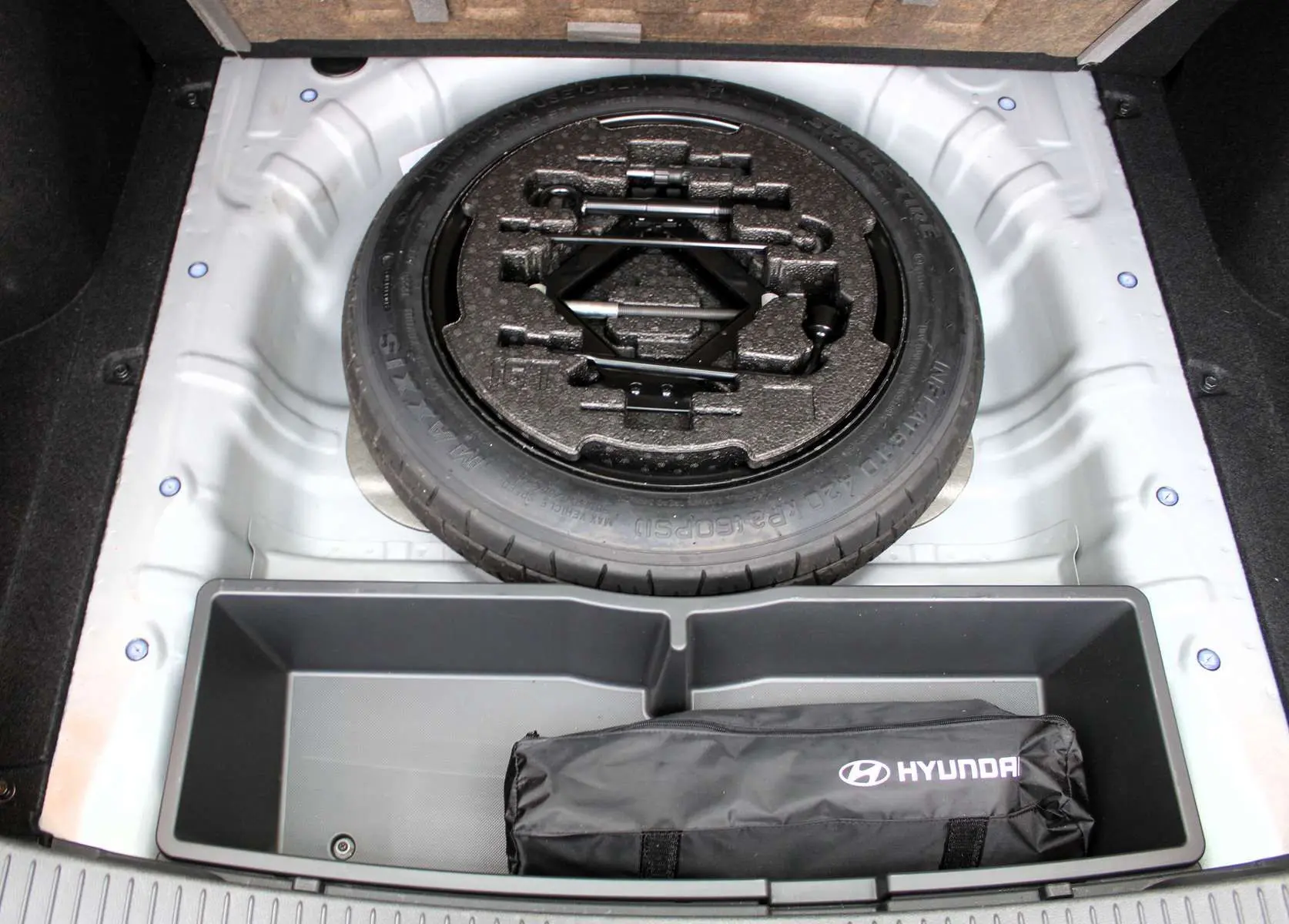 Vue plongeante sur la roue de secours et le rangement du coffre d'une Hyundai i30 SW 2024 couleur argent scintillant.