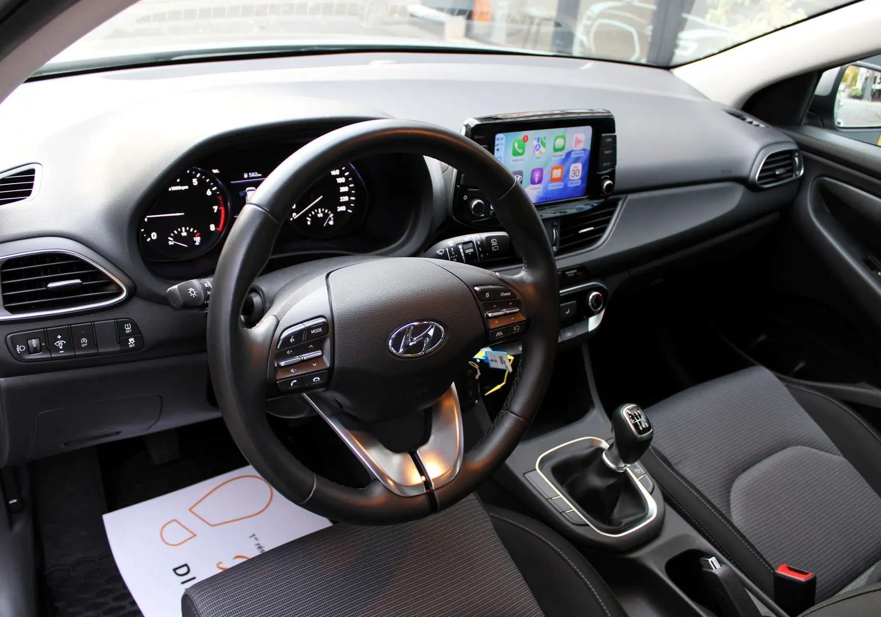 Intérieur de la Hyundai i30 SW 2024, vue du poste de conduite avec volant multifonction et écran tactile central.