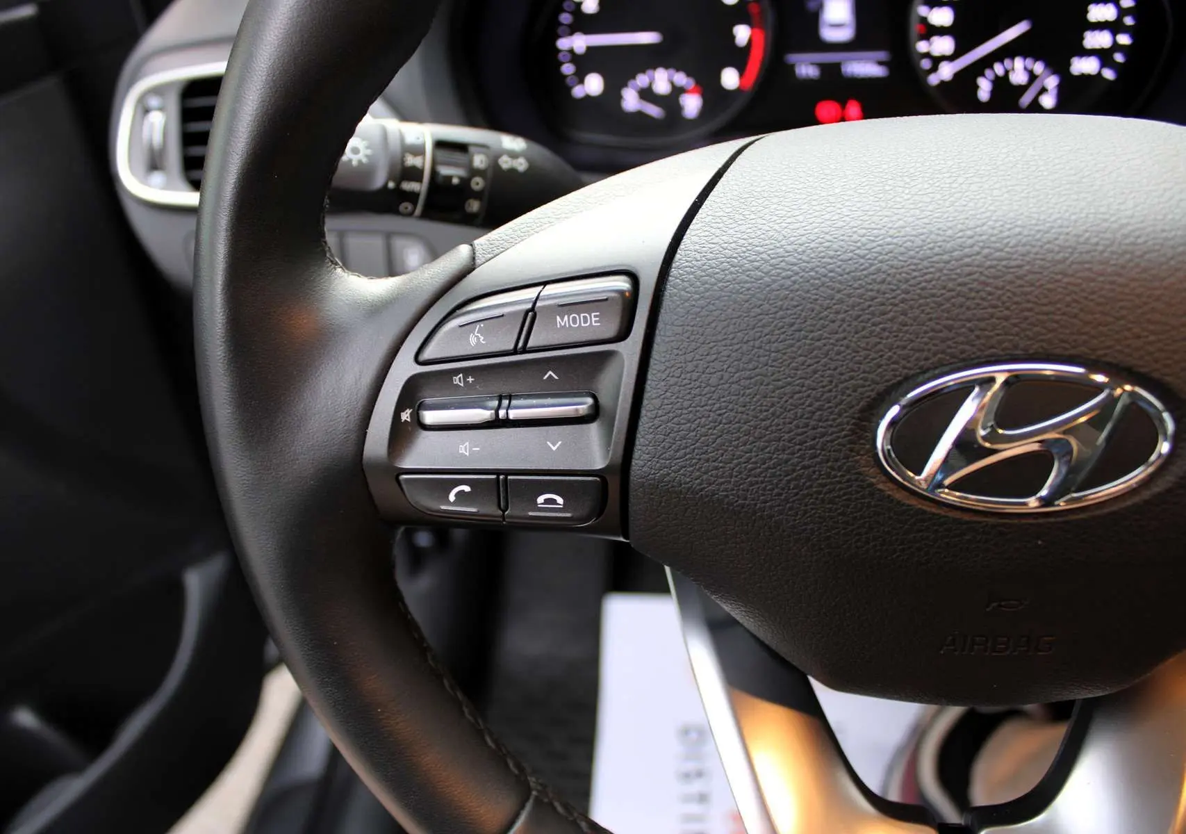 Gros plan sur le volant cuir noir de la Hyundai i30 SW 2024 avec commandes audio intégrées côté gauche.