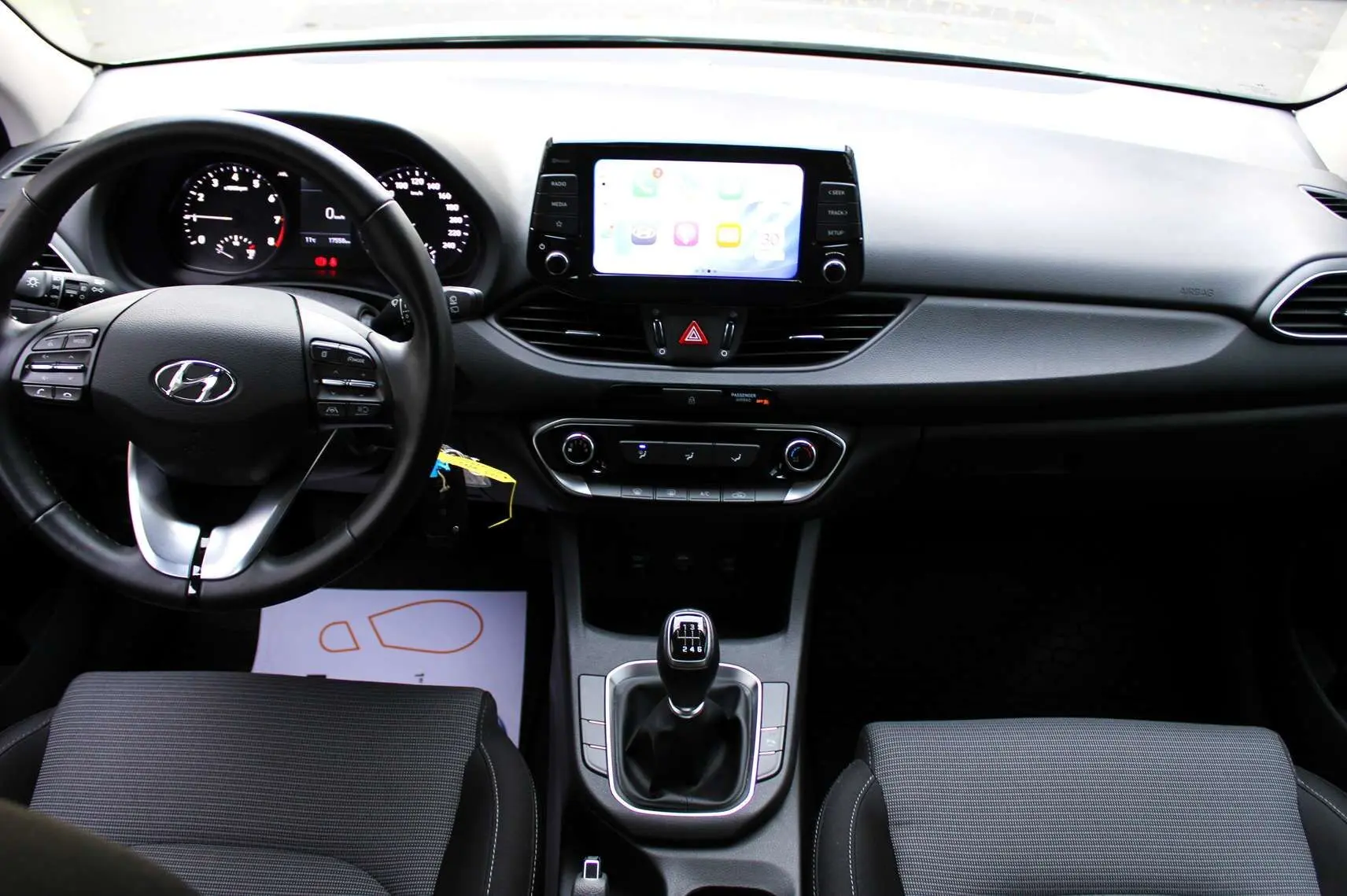 Vue intérieure avant de la Hyundai i30 SW 2024 avec tableau de bord noir et levier de vitesse manuel visible.