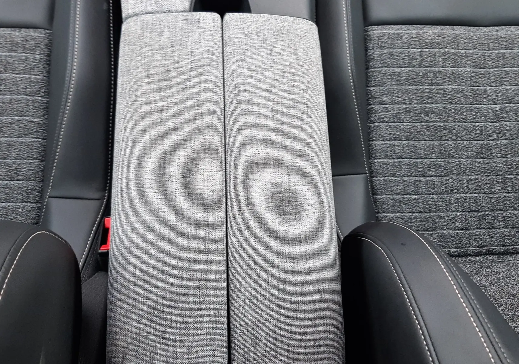 Vue plongeante sur l'accoudoir central gris tissu et les sièges noirs avec surpiqûres blanches du Peugeot 3008 Hybrid 2025.