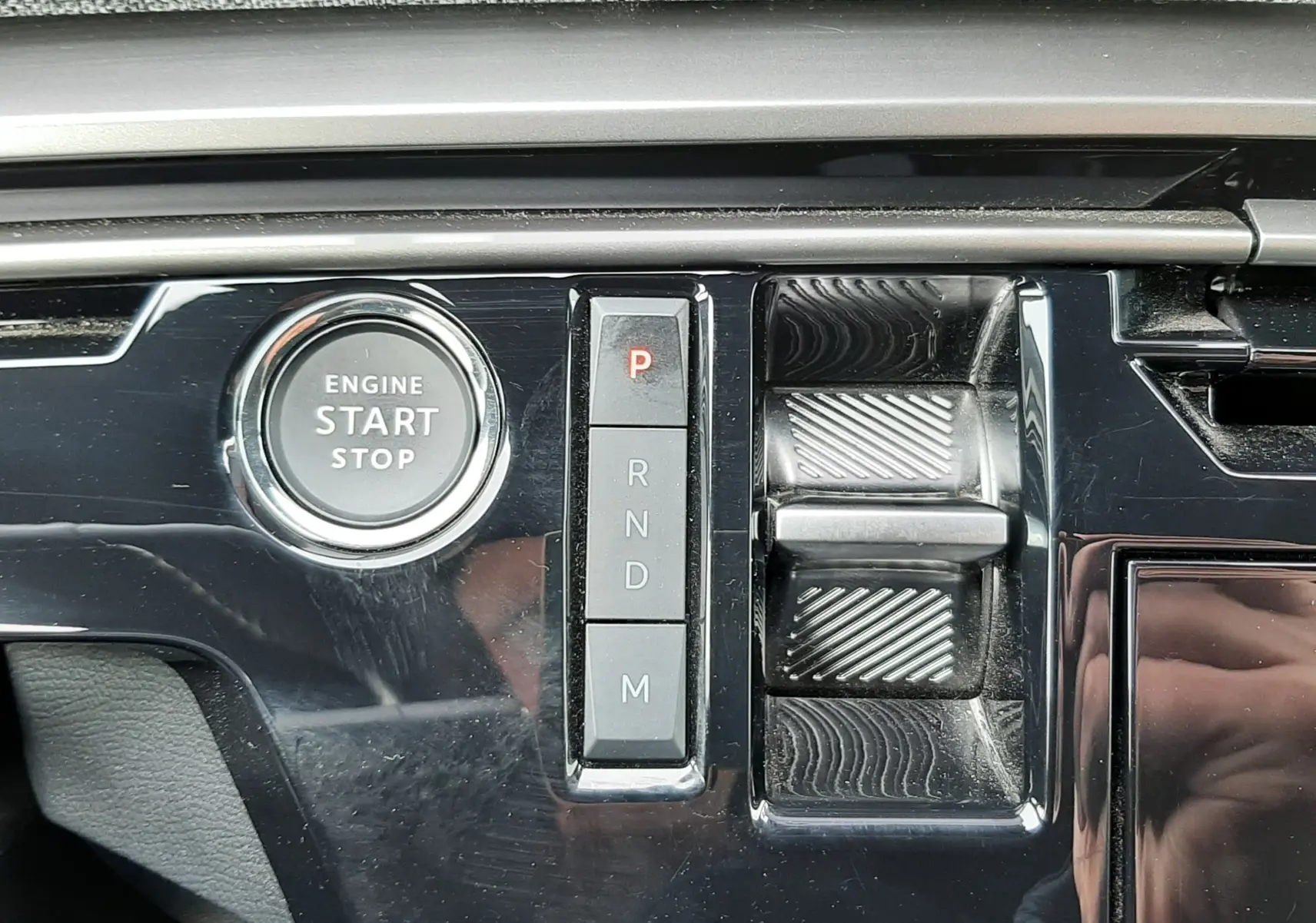 Gros plan sur la console centrale noire brillante du Peugeot 3008 III Hybrid 145 Allure avec bouton start/stop et commandes de boîte auto.