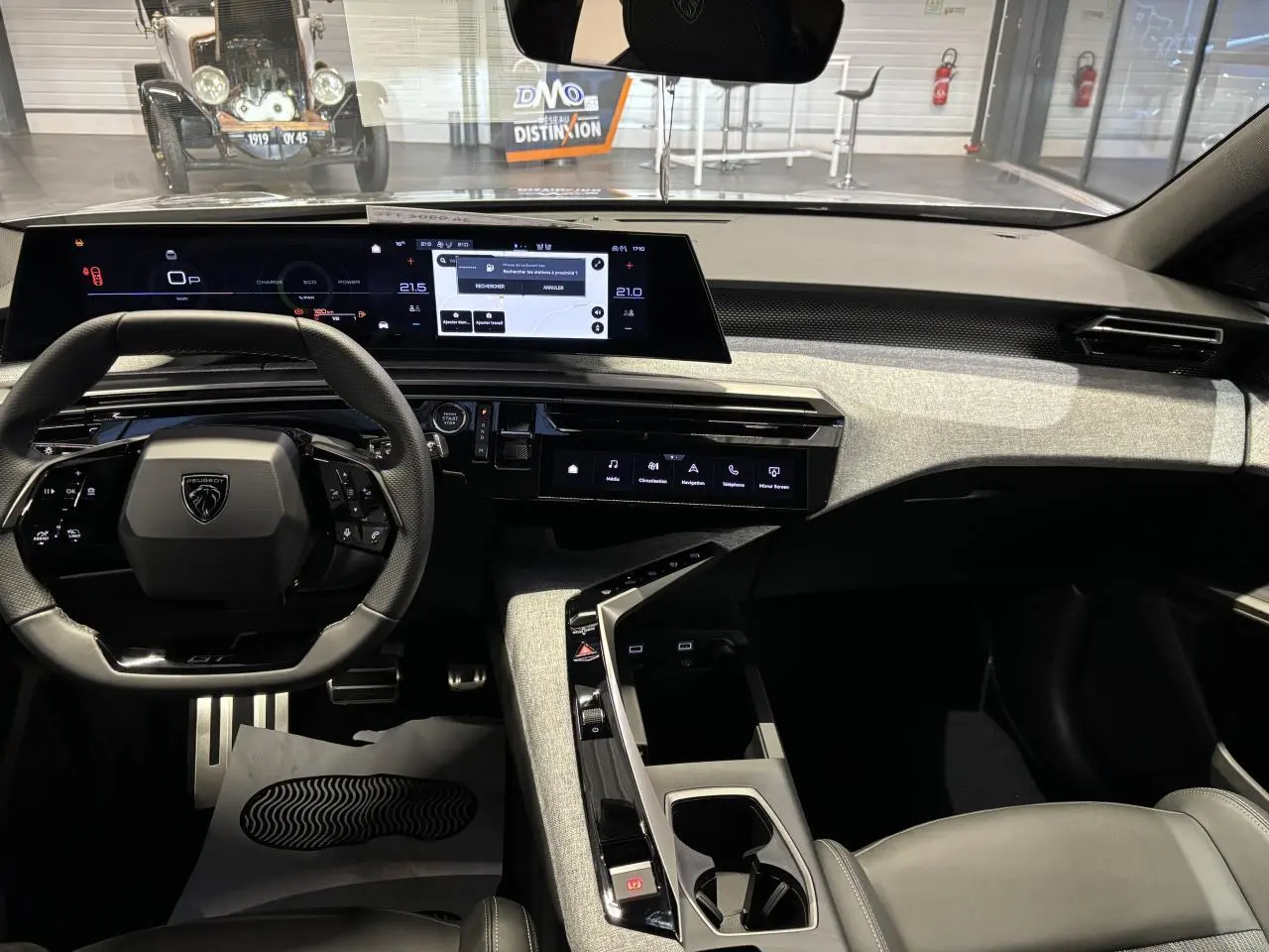 Vue intérieure avant du Peugeot 3008 Hybrid 2025, tableau de bord moderne avec écran panoramique et volant compact noir.