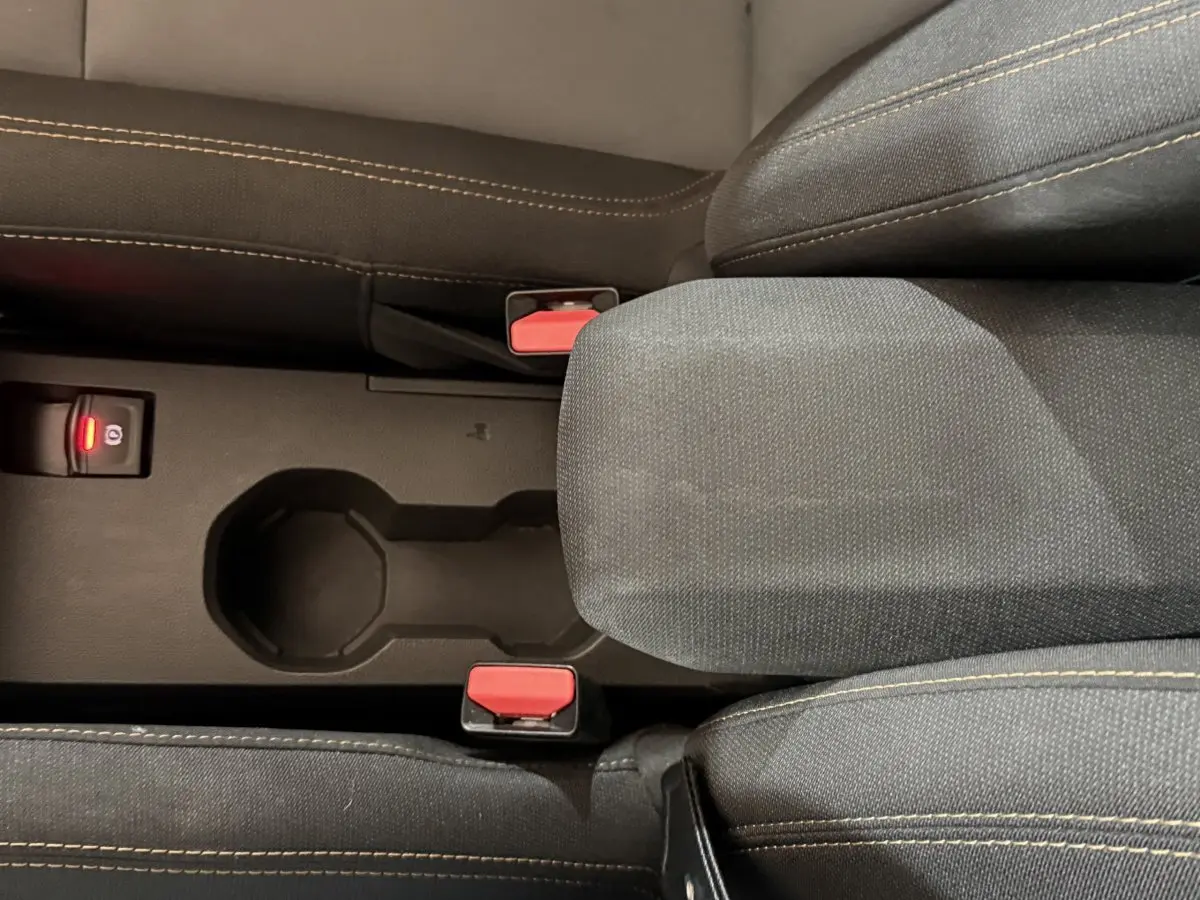 Vue rapprochée de la console centrale noire avec accoudoir tissu et boutons de frein à main électrique sur Dacia Sandero Extreme+ vert.