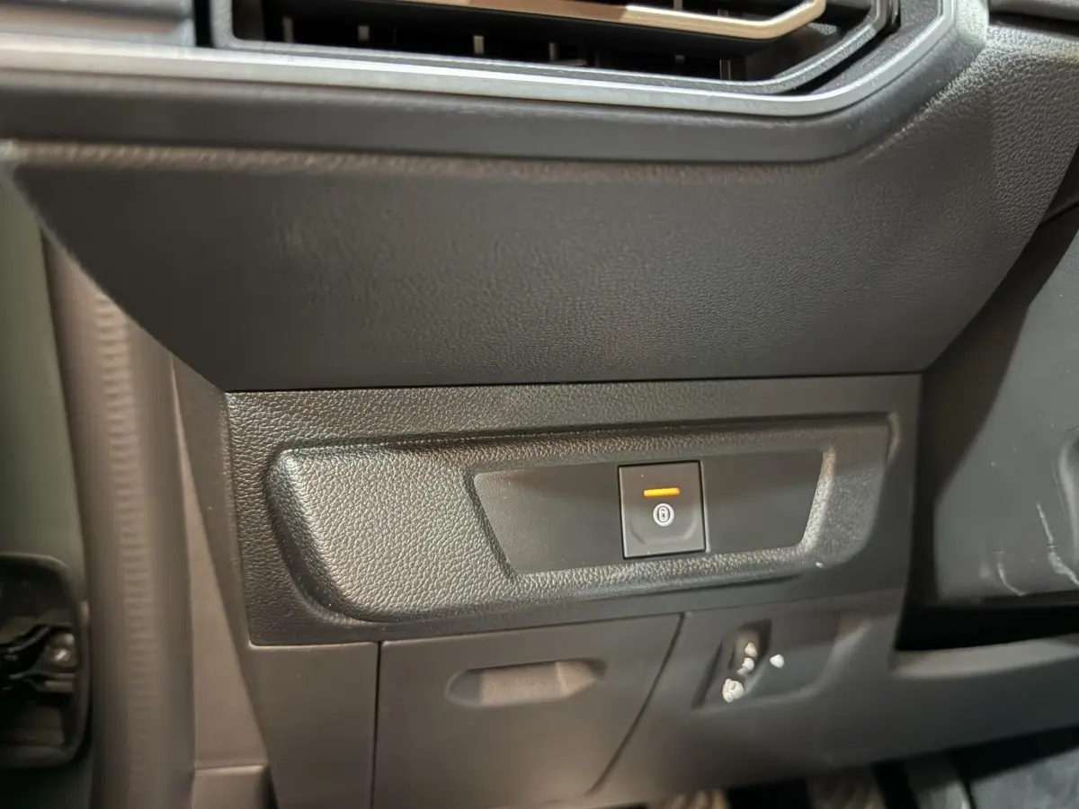 Gros plan sur le bouton de frein à main électrique orange dans l'habitacle noir de la Dacia Sandero Extreme+ 2024.