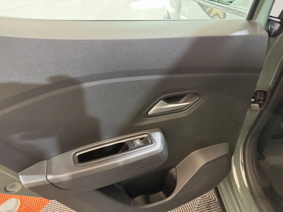 Vue intérieure côté gauche de la porte avant verte d'une Dacia Sandero Extreme+ avec commande de vitre électrique.