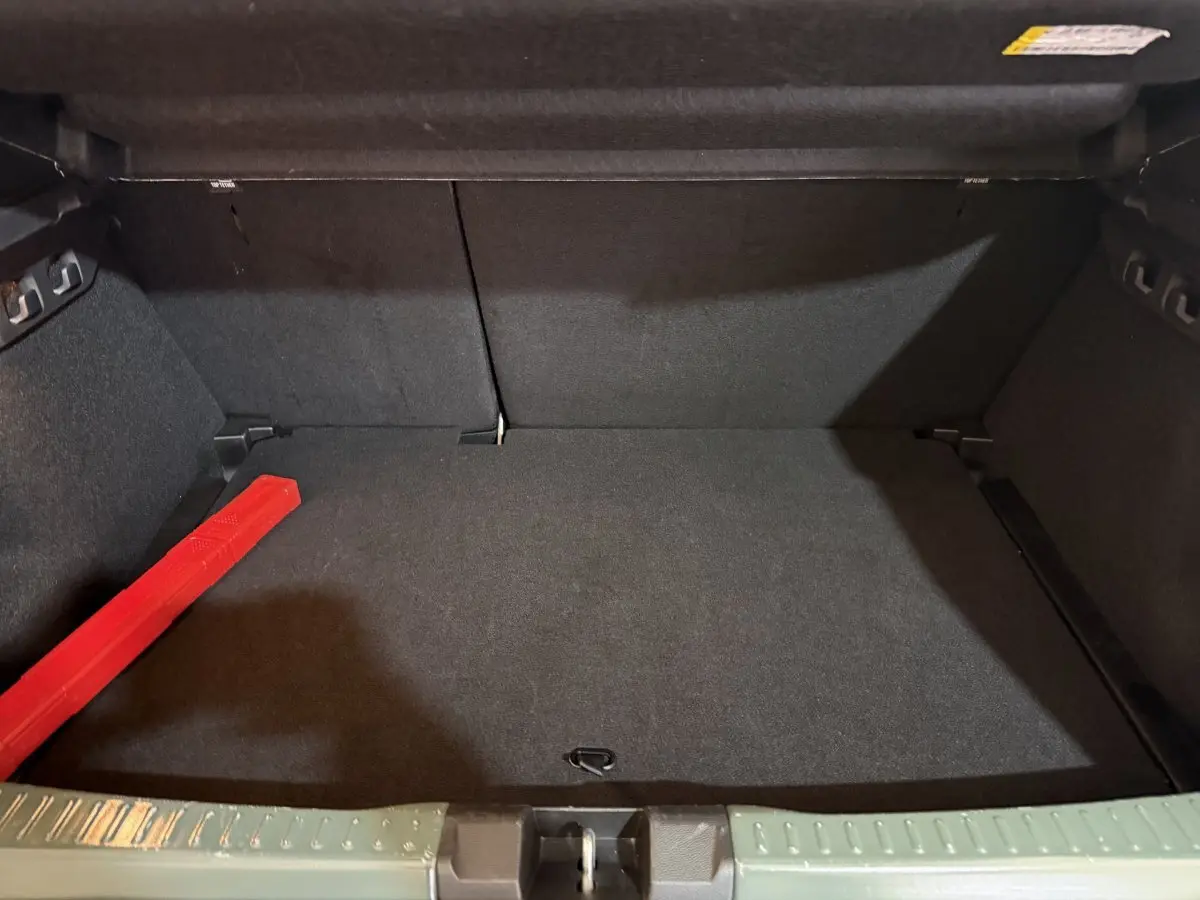 Coffre ouvert de la Dacia Sandero Extreme+ TCe 110 2024 vert, avec tapis noir et triangle de signalisation rouge.