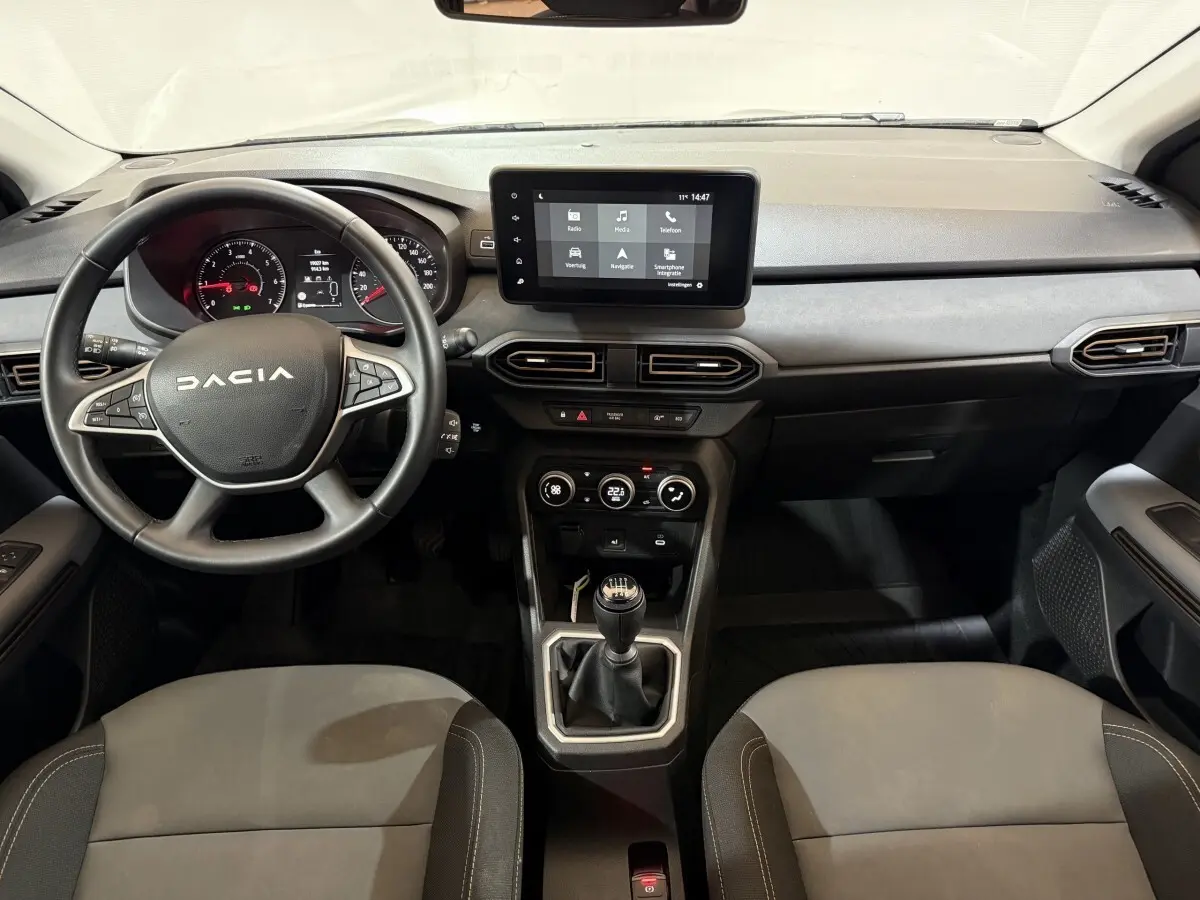 Vue intérieure avant de la Dacia Sandero 2024, volant multifonctions cuir, écran tactile central et levier de vitesse manuel.