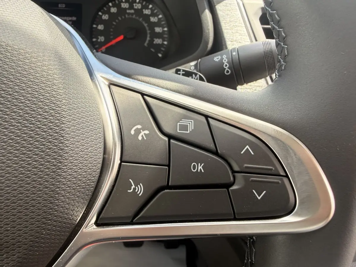 Gros plan sur les commandes multifonctions noires du volant réglable du Renault Trafic Fourgon blanc, tableau de bord en arrière-plan.