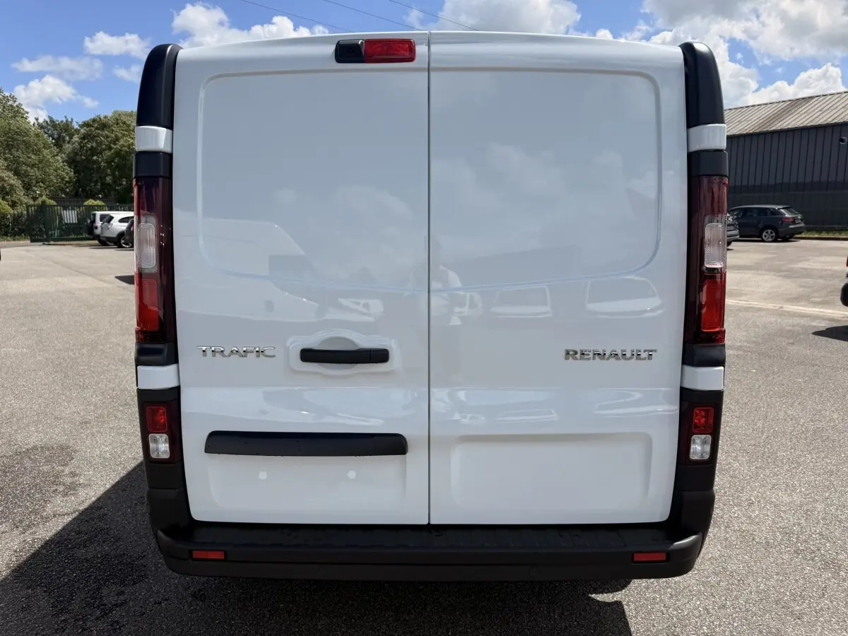 Vue arrière d’un Renault Trafic fourgon blanc avec portes battantes et feux arrière verticaux rouges et blancs.