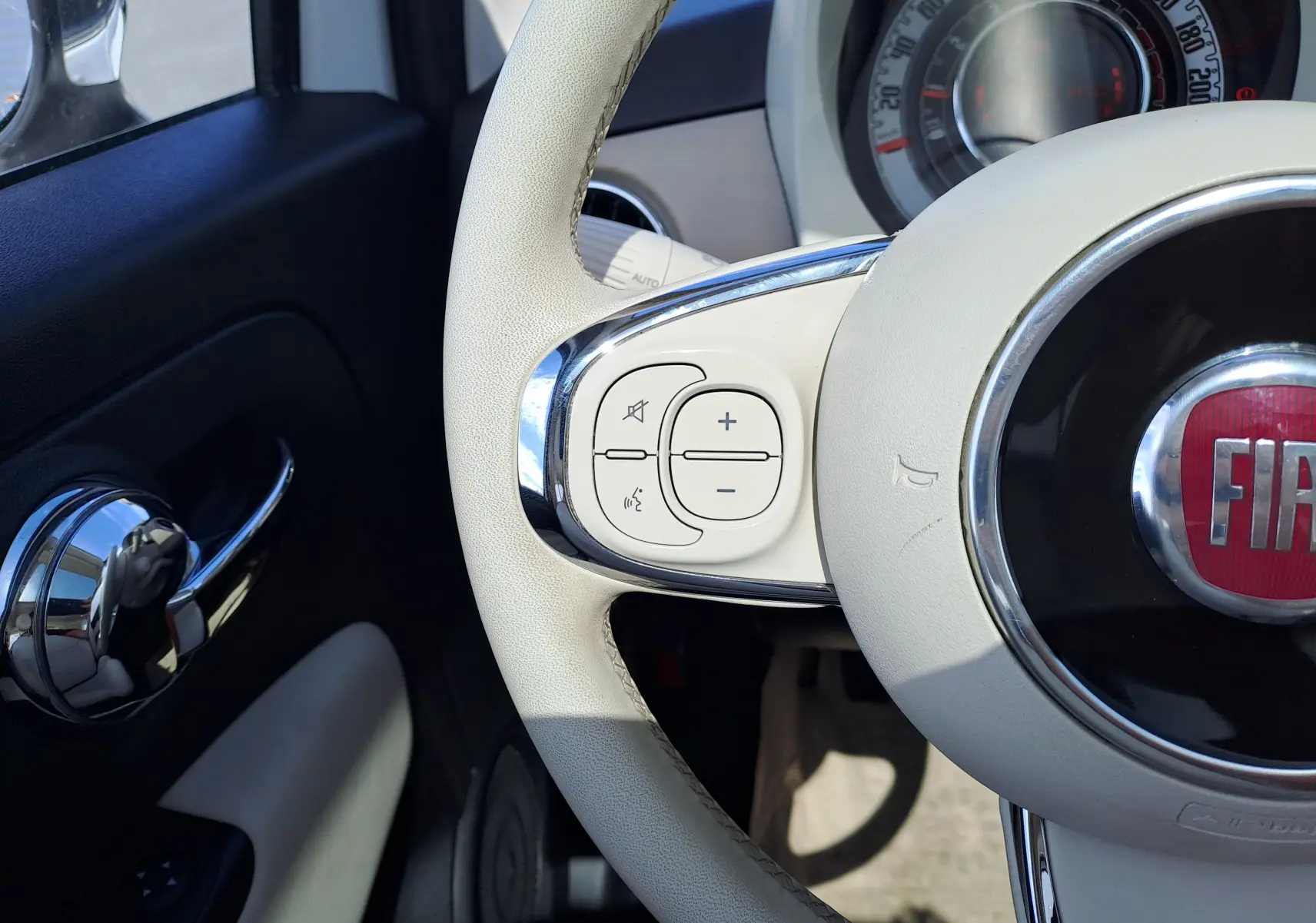 Gros plan sur le volant beige de la Fiat 500 1.0 Hybrid 70ch DolceVita avec commandes audio intégrées.