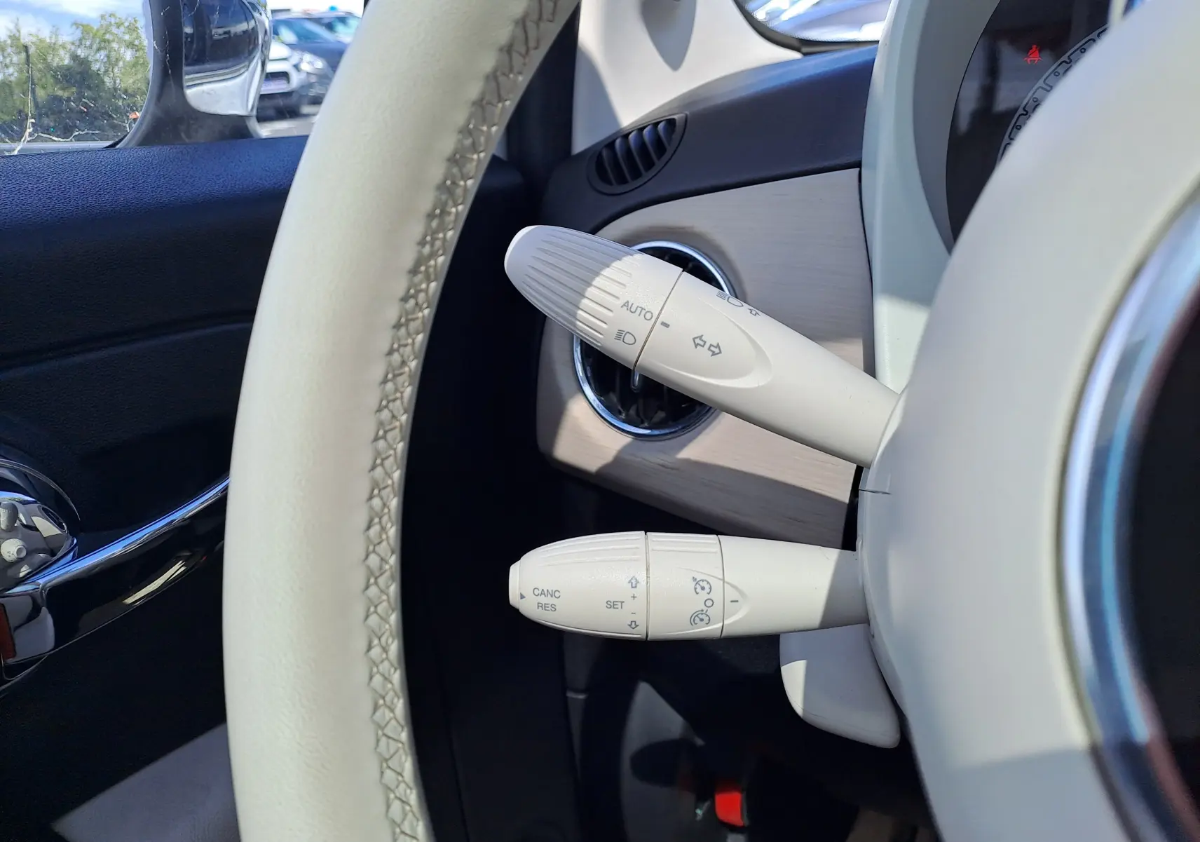 Gros plan sur les commandes blanches du volant d'une FIAT 500 blanche, intérieur beige et noir visible côté gauche.