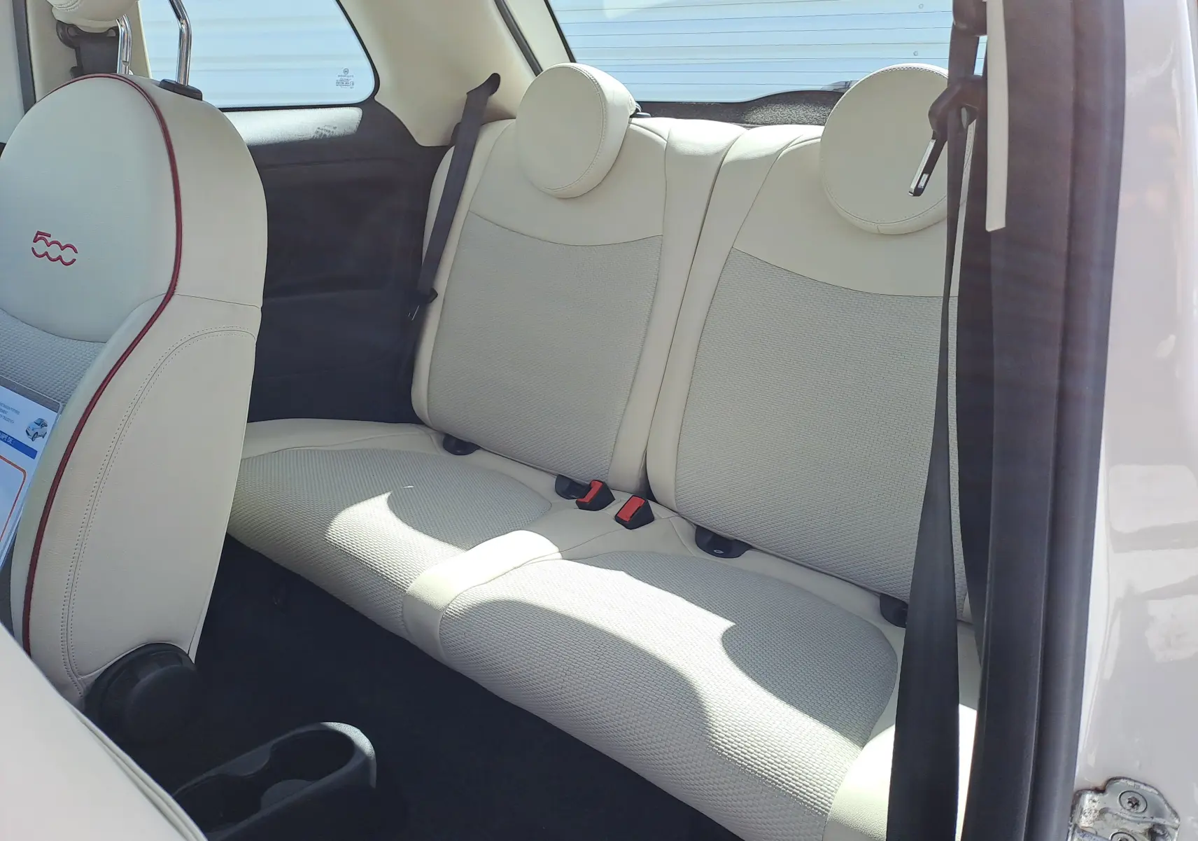 Vue intérieure côté arrière droit de la Fiat 500 blanche, sièges arrière en cuir beige clair avec appuie-têtes ronds.