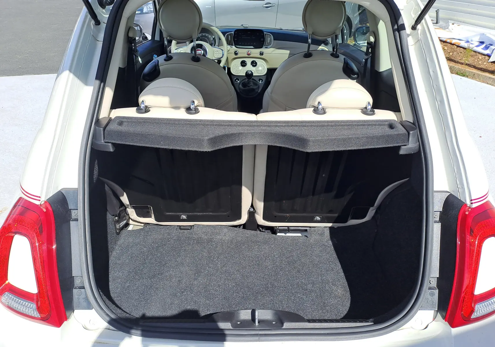 Coffre ouvert d'une FIAT 500 blanche vue de l'arrière, montrant l'intérieur beige clair et le tableau de bord compact.